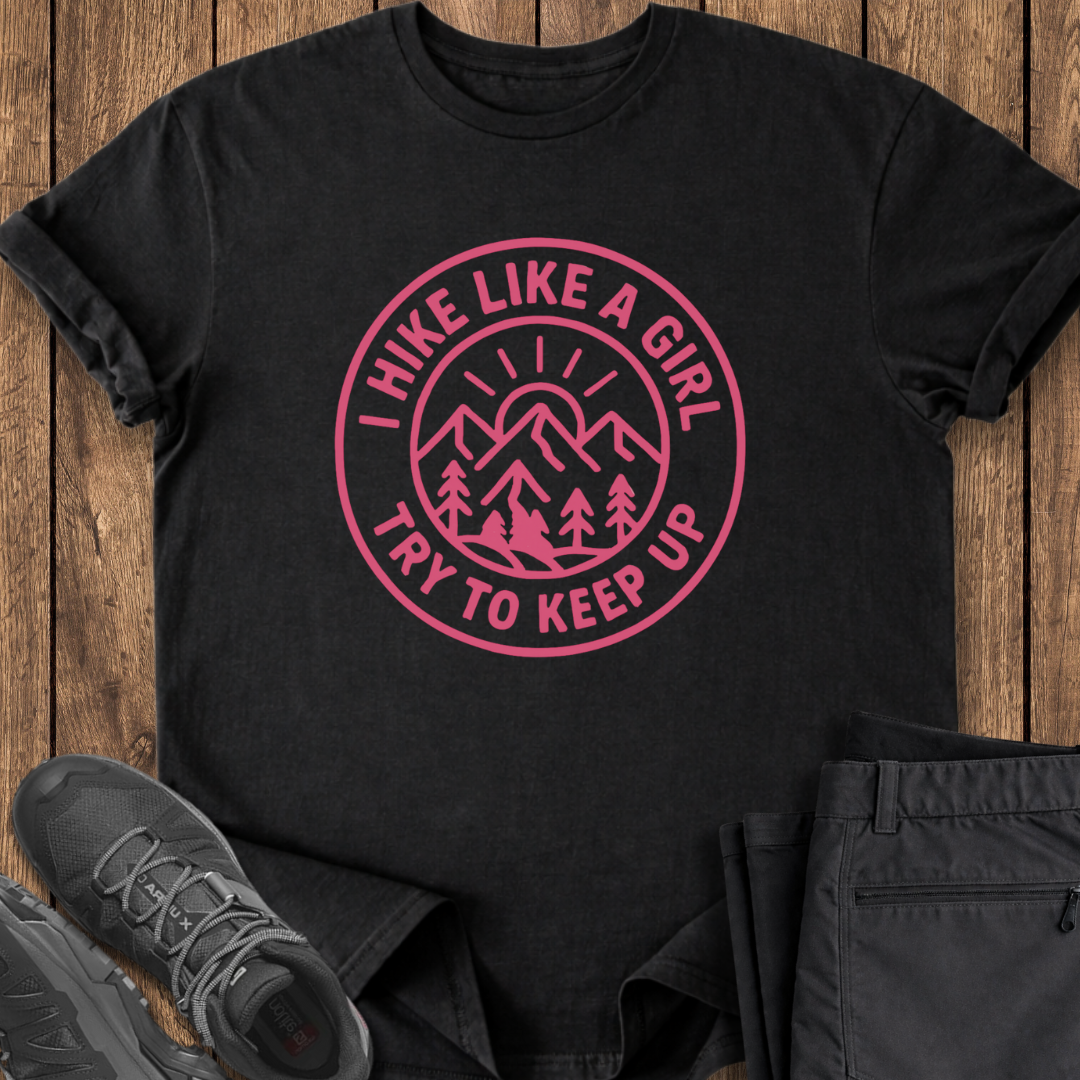 Black t-shirt with pink graphic and text on a wooden surface with shoes and pants.