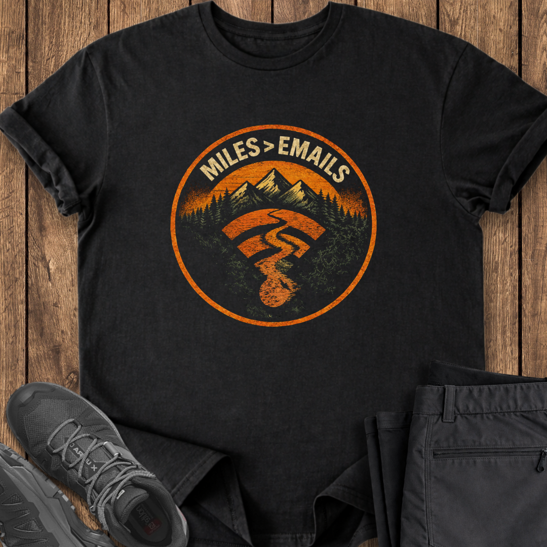 Black t-shirt with a mountain and nature graphic on a wooden surface with shoes and pants. hiking t shirt