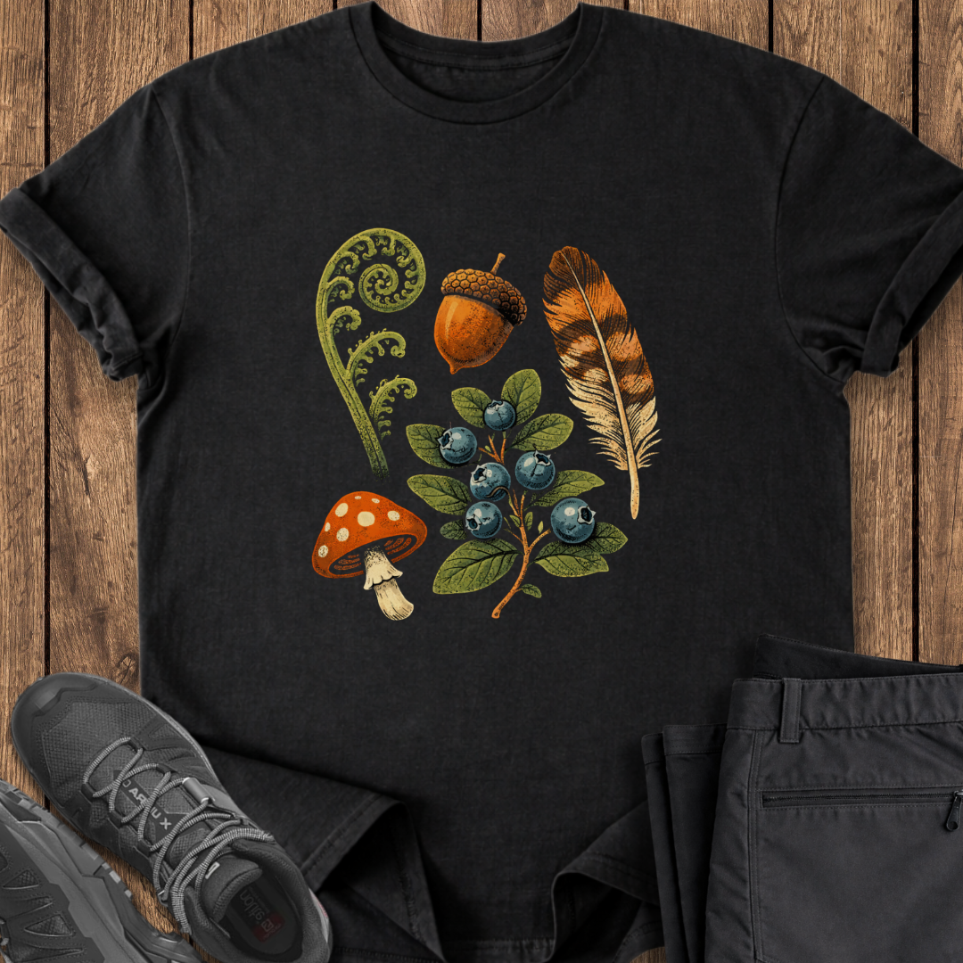 Black t-shirt with nature-themed design featuring a mushroom, acorn, feather, and blueberries on a wooden surface.