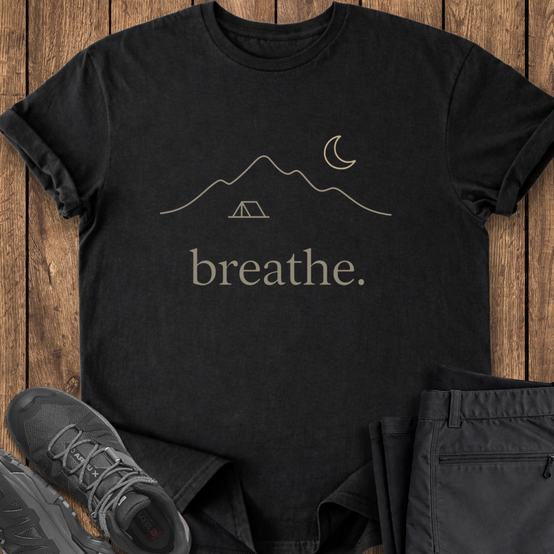 Black t-shirt with 'breathe.' design on a wooden surface with shoes and pants.