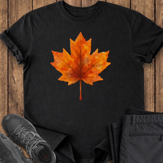 Black t-shirt with orange maple leaf design on a wooden surface with shoes and pants.