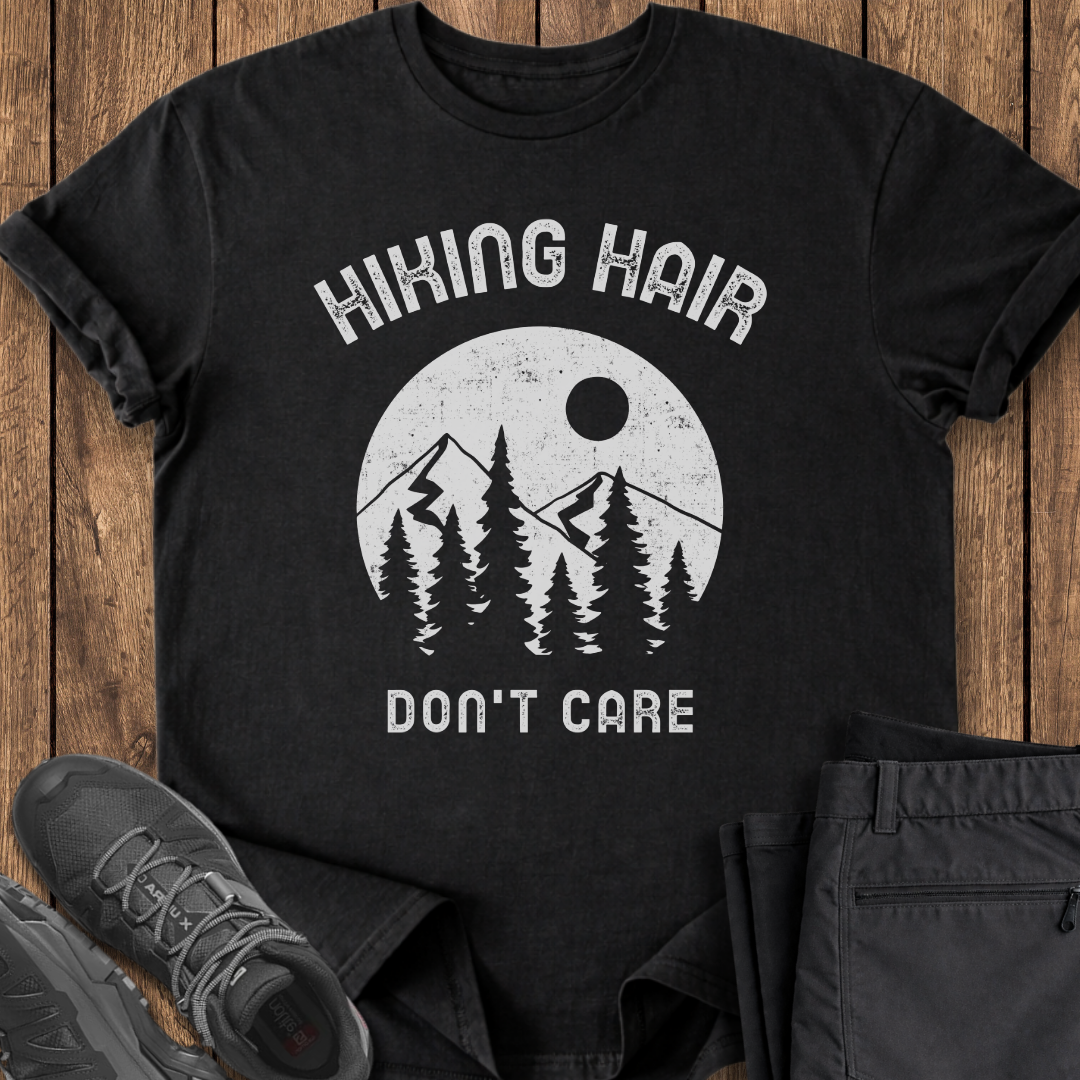 Black t-shirt with 'Hiking Hair Don't Care' graphic on a wooden surface with shoes and pants. funny hiking