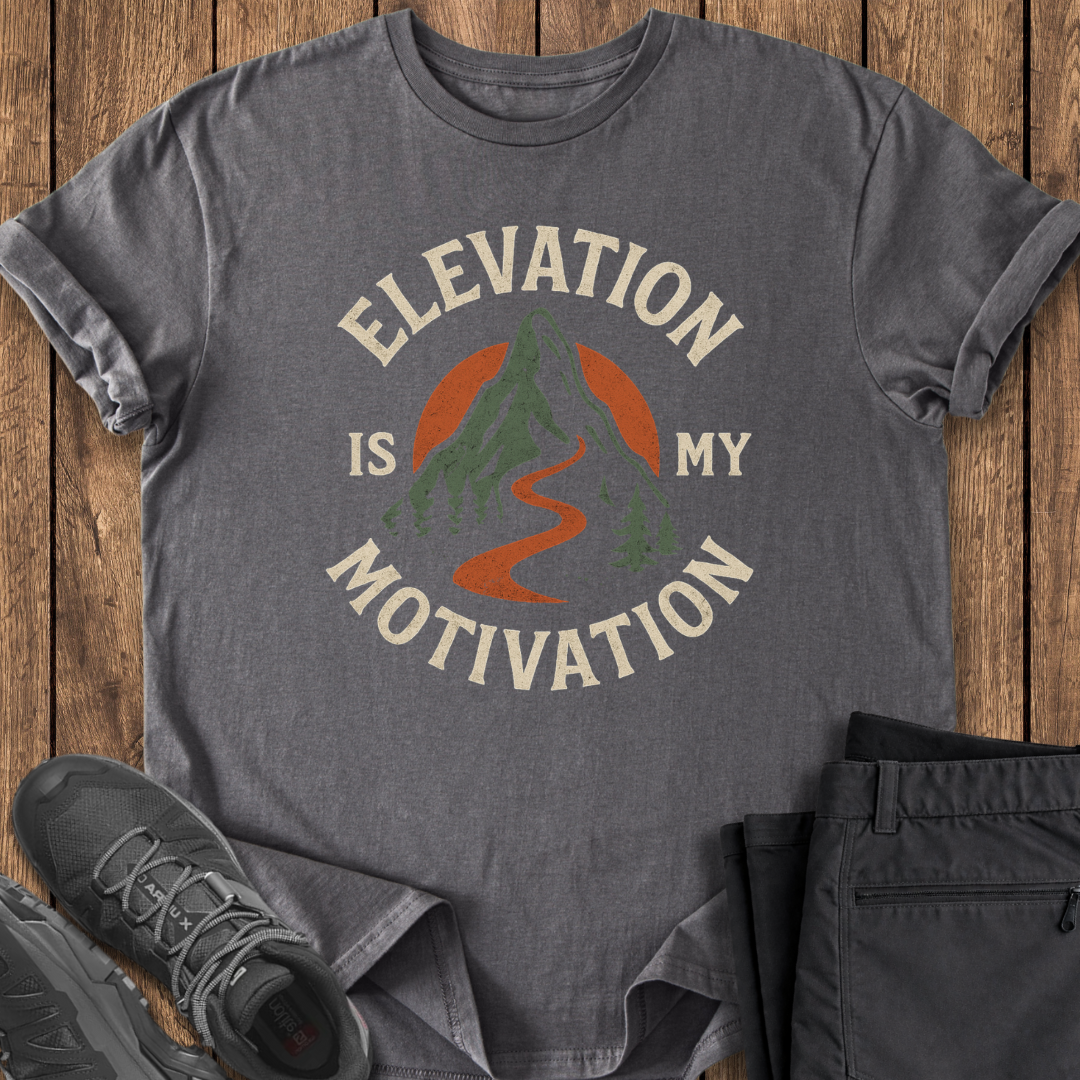 Gray t-shirt with 'Elevation is My Motivation' design on a wooden surface with shoes and pants. hiking mountaineering clibming t shirt