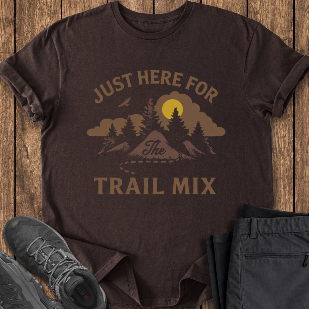 Brown t-shirt with 'Just Here for the Trail Mix' graphic on a wooden surface with shoes and shorts. funny trailmix hiking t shirt
