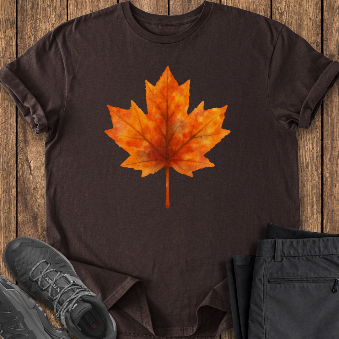 Brown t-shirt with orange maple leaf design on a wooden surface with shoes and pants.