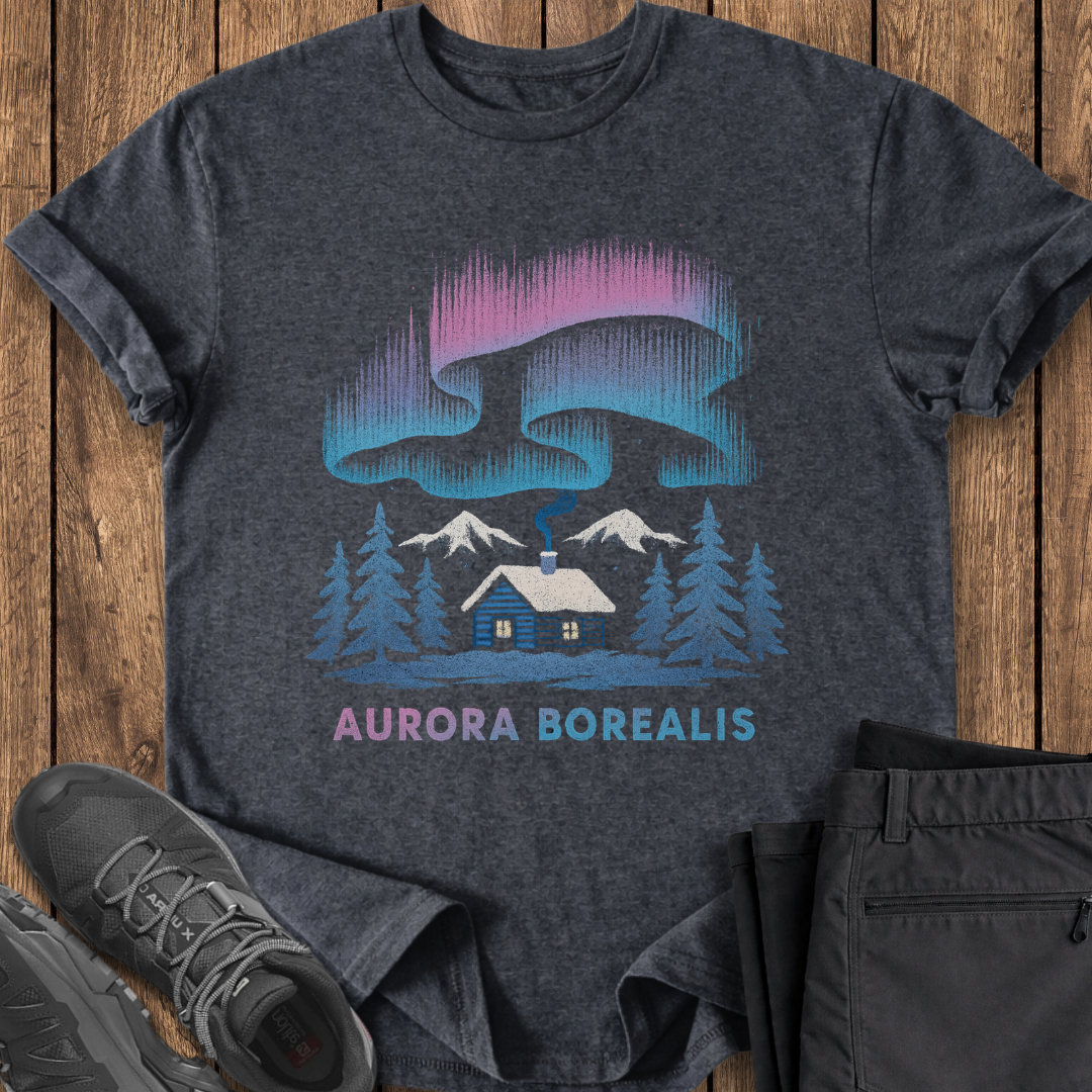 Dark gray t-shirt with 'Aurora Borealis' design featuring a cabin and trees on a wooden surface. northern lights winter cabin tee