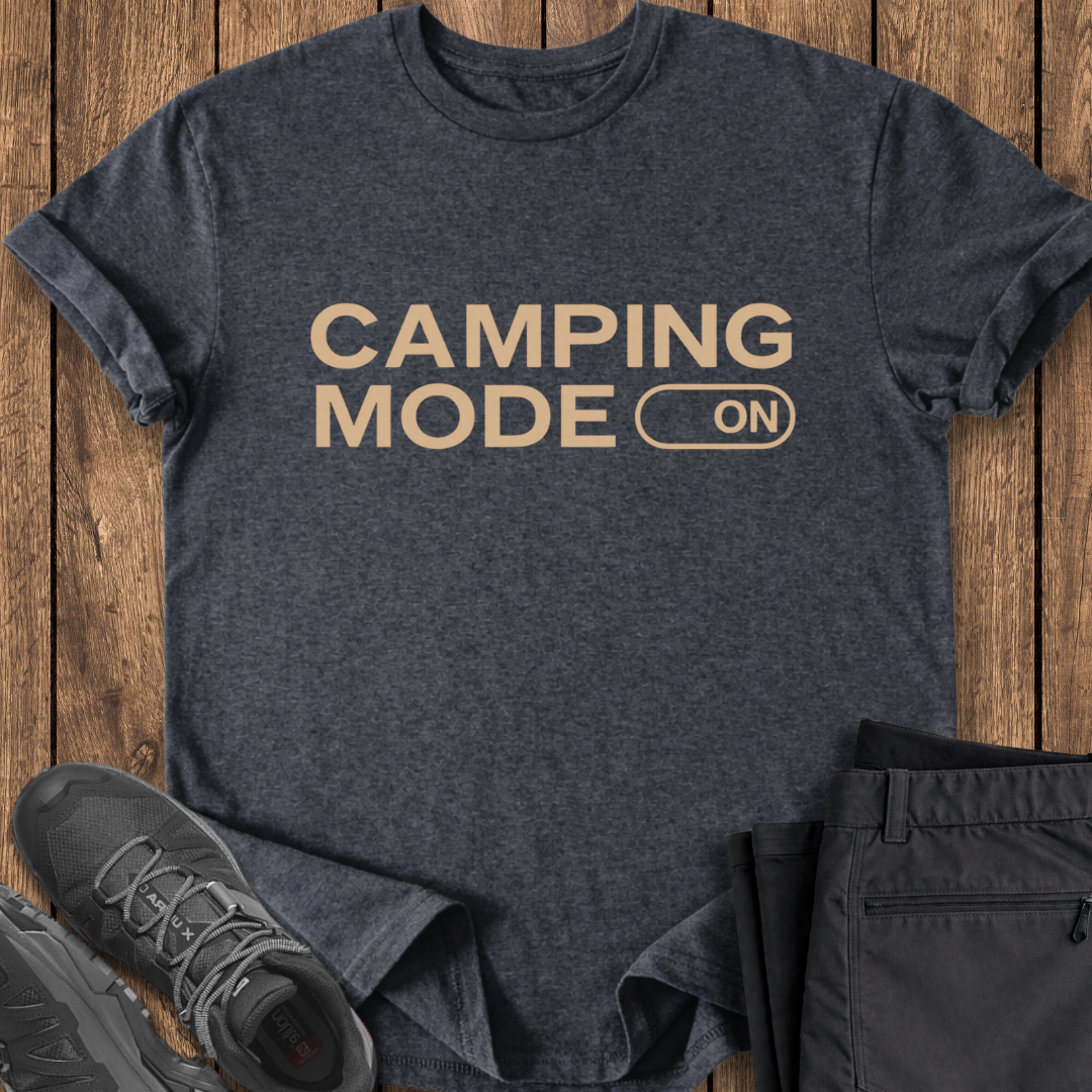 Dark gray t-shirt with 'Camping Mode On' text on a wooden surface, surrounded by camping-themed items.