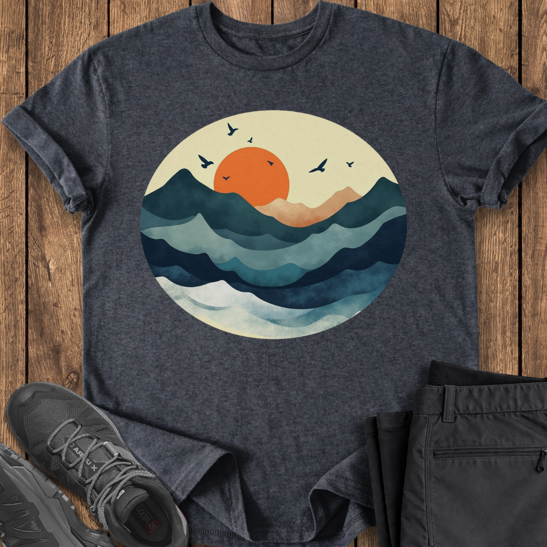 Dark gray t-shirt with a sunset and wave design on a wooden surface, accompanied by black pants and shoes.