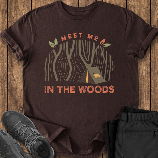 Brown t-shirt with 'Meet Me in the Woods' design on a wooden surface with shoes and pants. camping t shirt