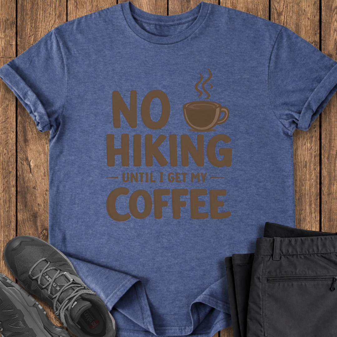 Blue t-shirt with 'No Hiking Until I Get My Coffee' text and graphic on a wooden surface with shoes and shorts. funny hiking coffee t shirt