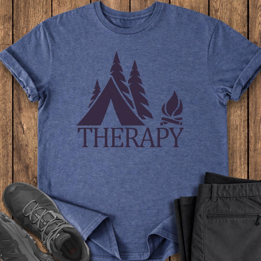 Blue t-shirt with 'THERAPY' and camping graphic on a wooden surface, with shoes and pants.