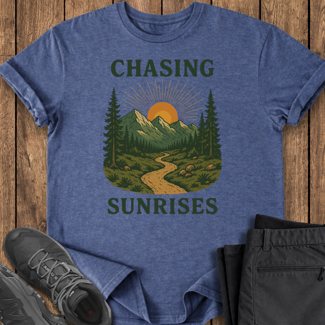 Blue t-shirt with nature graphic and text 'Chasing Sunrises' on a wooden surface with shoes and shorts.
