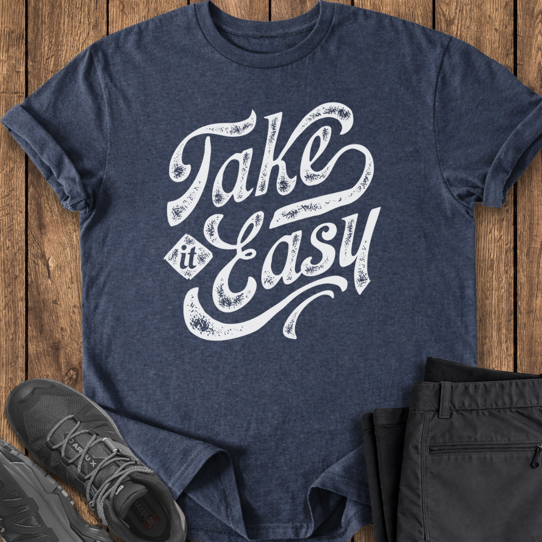 Navy blue t-shirt with 'Take It Easy' text on a wooden surface with shoes and pants.