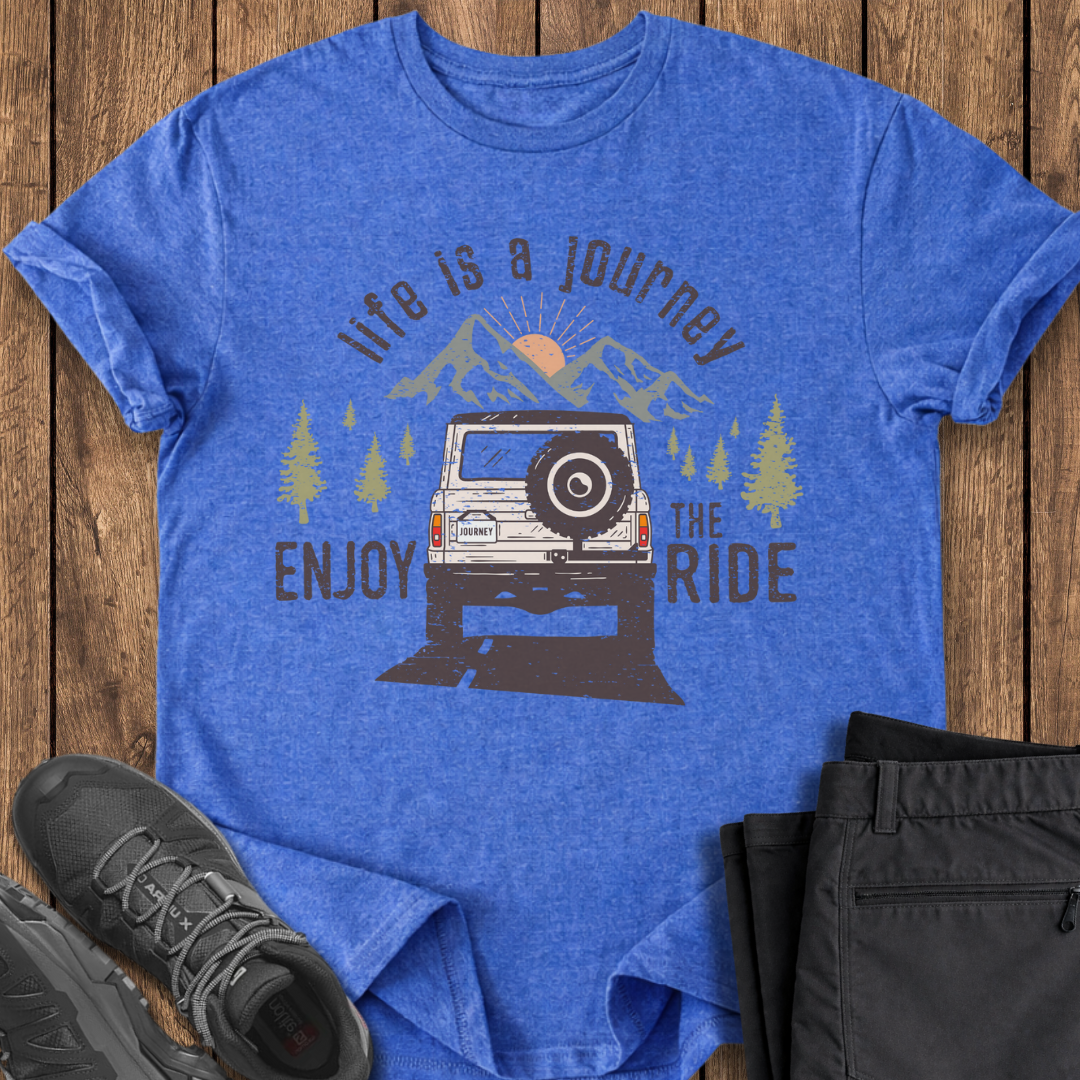 Blue t-shirt with graphic design of a jeep and text 'Life is a Journey, Enjoy the Ride' on a wooden surface.