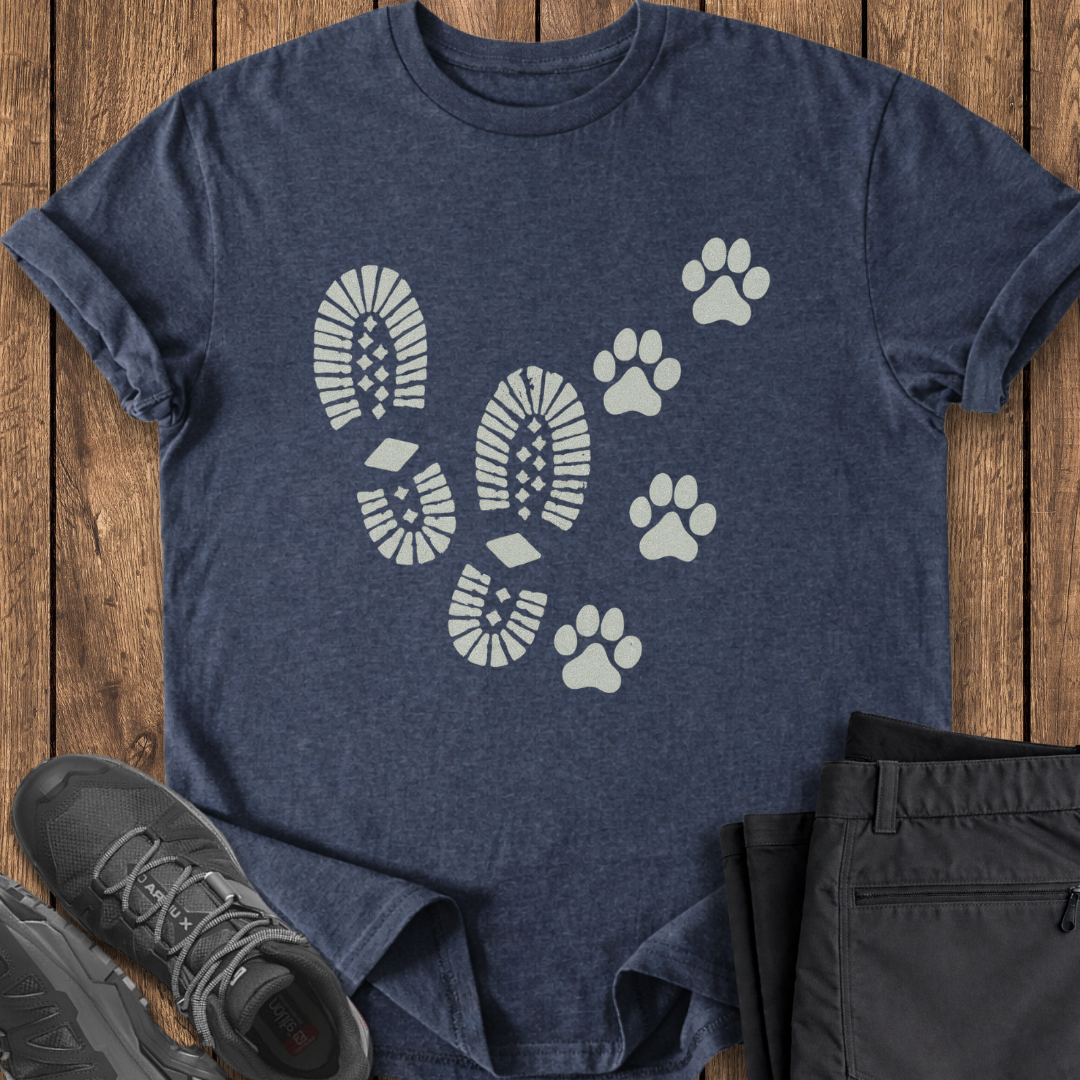 Navy blue t-shirt with white paw and footprint design on a wooden surface, with black shoes and pants.