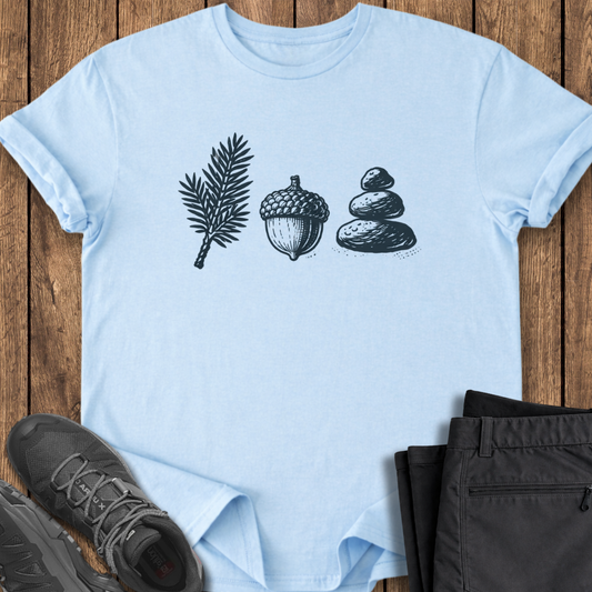 Light blue t-shirt with nature-themed design on a wooden surface with shoes and pants. hiking camping t shirt