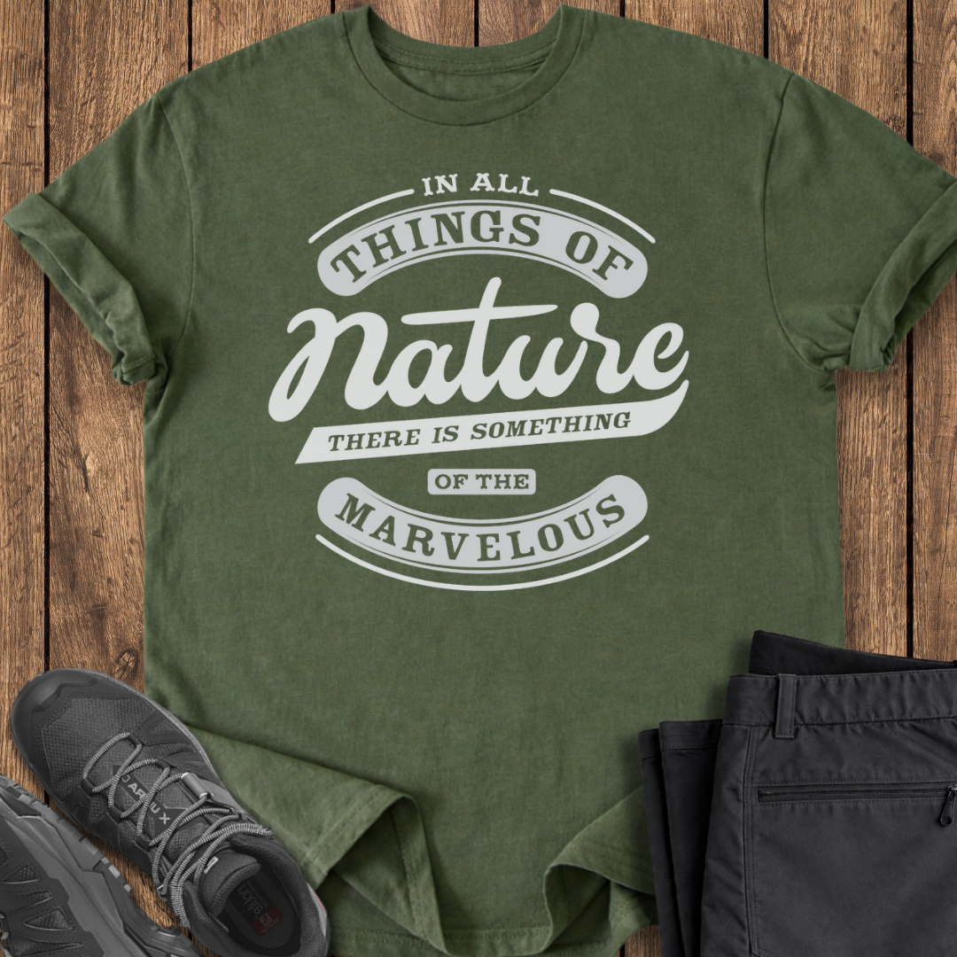 Green t-shirt with nature-themed text on a wooden surface with shoes and pants.