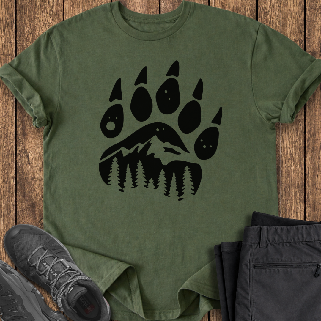 Green t-shirt with black bear paw print design on a wooden surface with shoes and pants. mountain bear