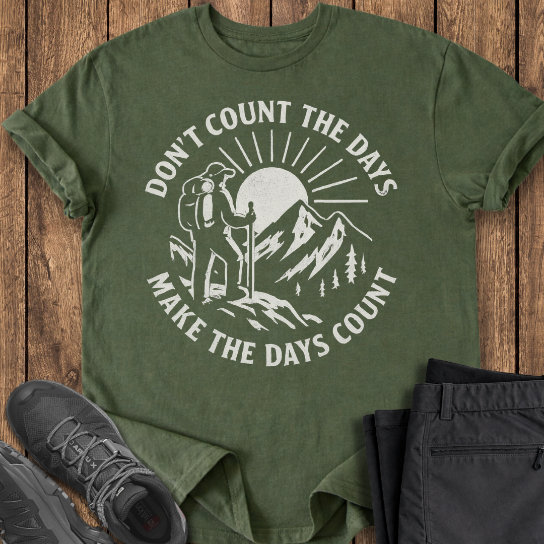Green t-shirt with outdoor design and text on a wooden surface with shoes and pants.