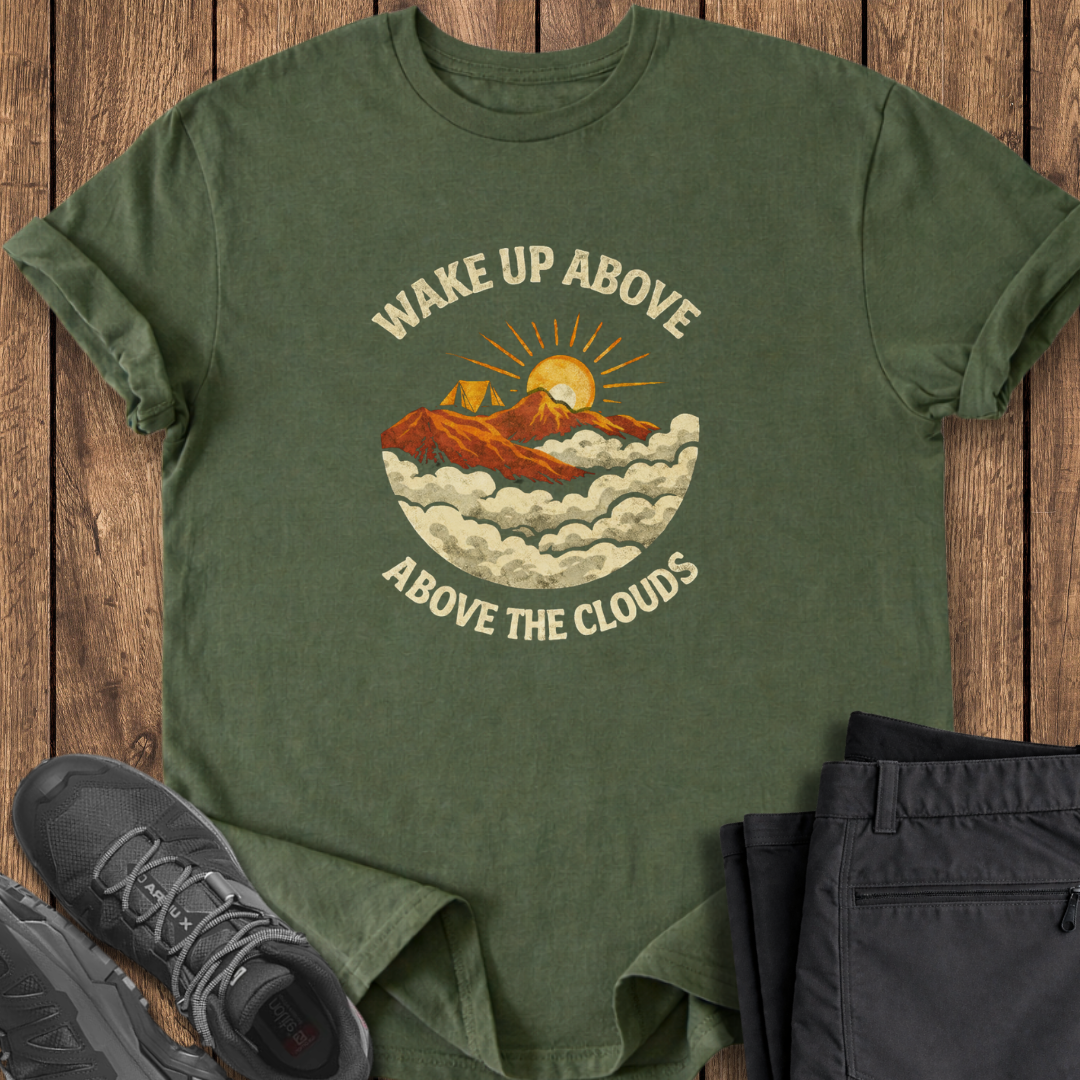 Green t-shirt with mountain graphic and text on a wooden surface with shoes and pants. mountaineering t shirt hiking