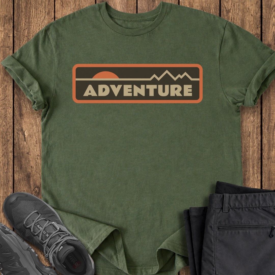 Green t-shirt with 'ADVENTURE' graphic on a wooden surface with shoes and pants.