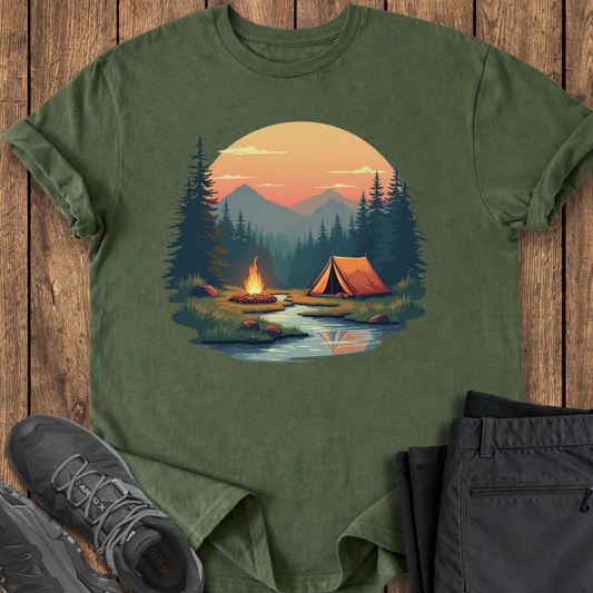 Green t-shirt with a camping scene design on a wooden surface with shoes and pants.