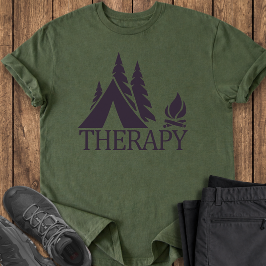 Green t-shirt with camping graphic and 'THERAPY' text on a wooden surface, with shoes and pants.
