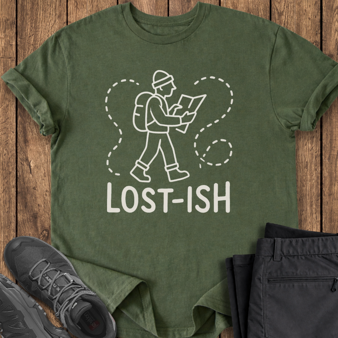 Green t-shirt with 'LOST-ISH' graphic on a wooden surface with shoes and pants.