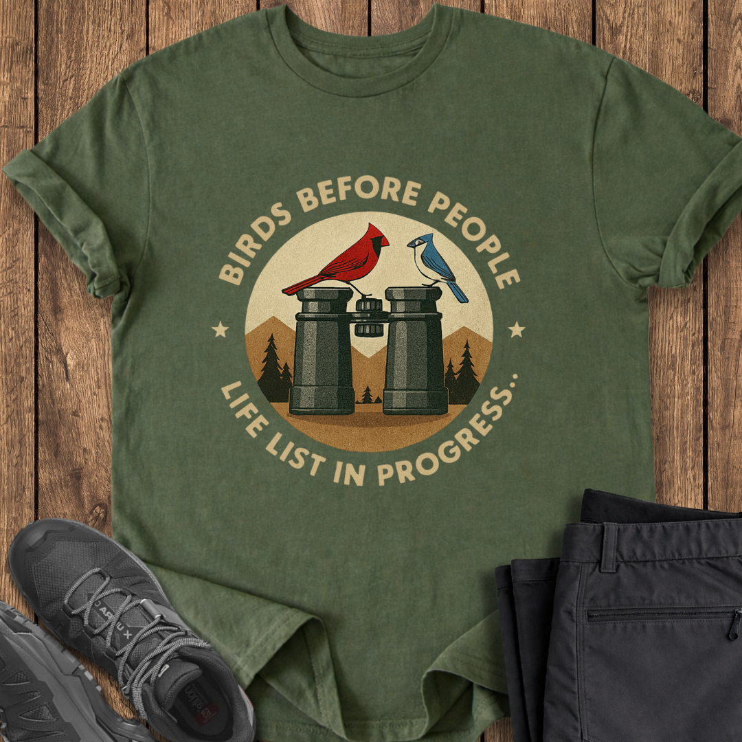 Green t-shirt with 'Birds Before People' graphic on a wooden surface with shoes and pants.