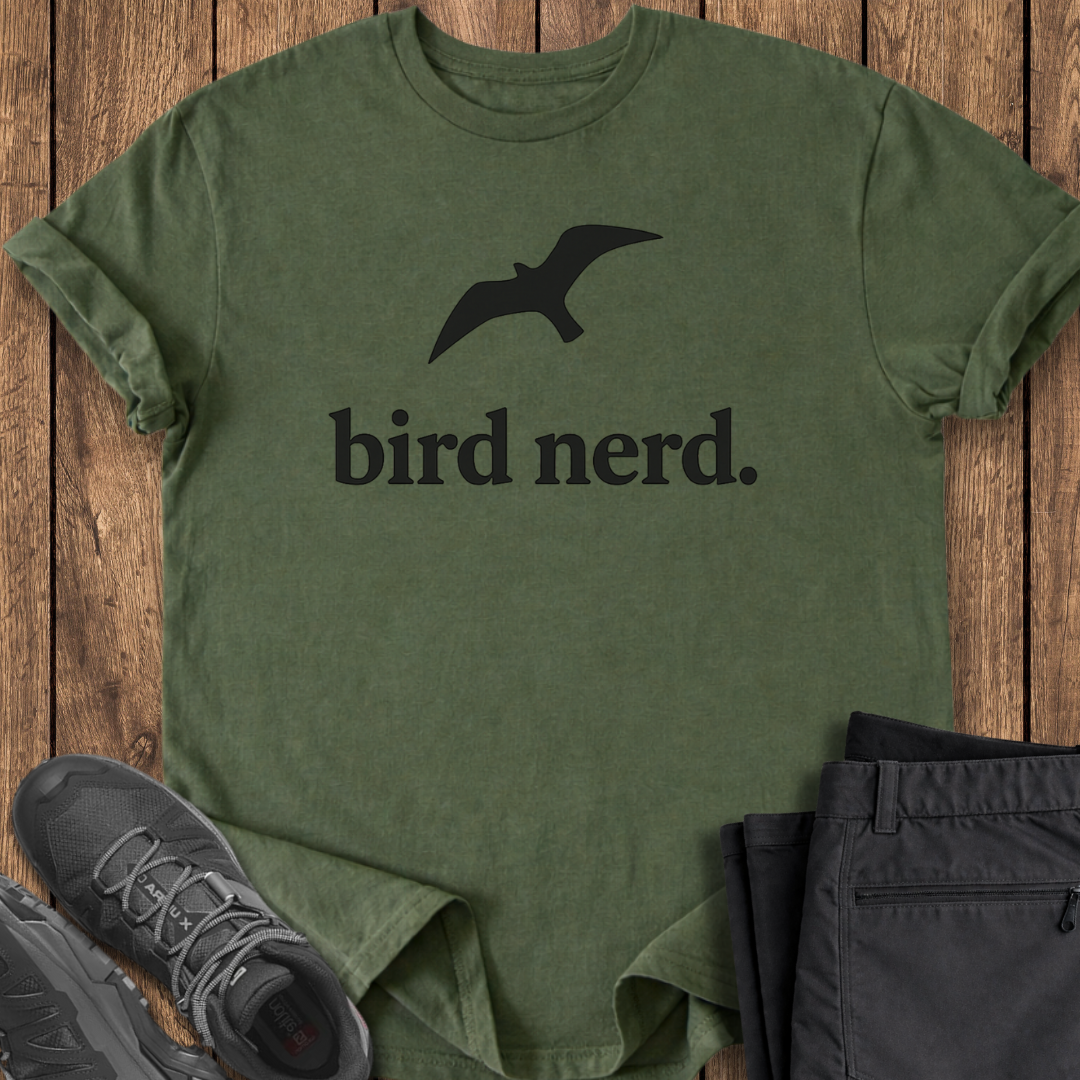 Green t-shirt with 'bird nerd.' text and a bird graphic on a wooden surface, with shoes and pants partially visible.