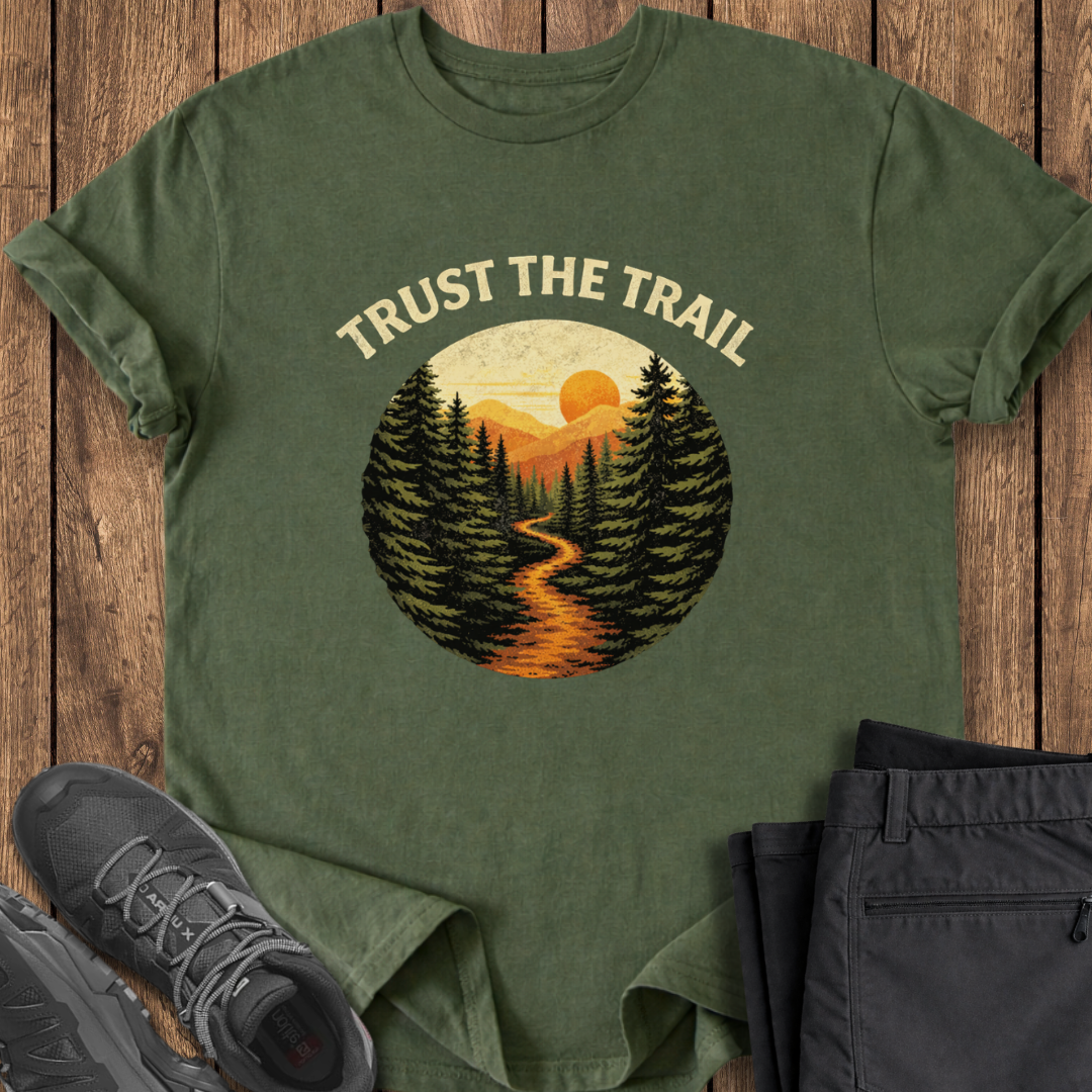Green t-shirt with 'Trust the Trail' graphic on a wooden surface with shoes and pants.