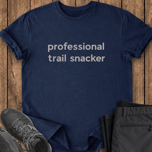 Navy blue t-shirt with 'professional trail snacker' text on a wooden surface with shoes and shorts. funny hike t shirt