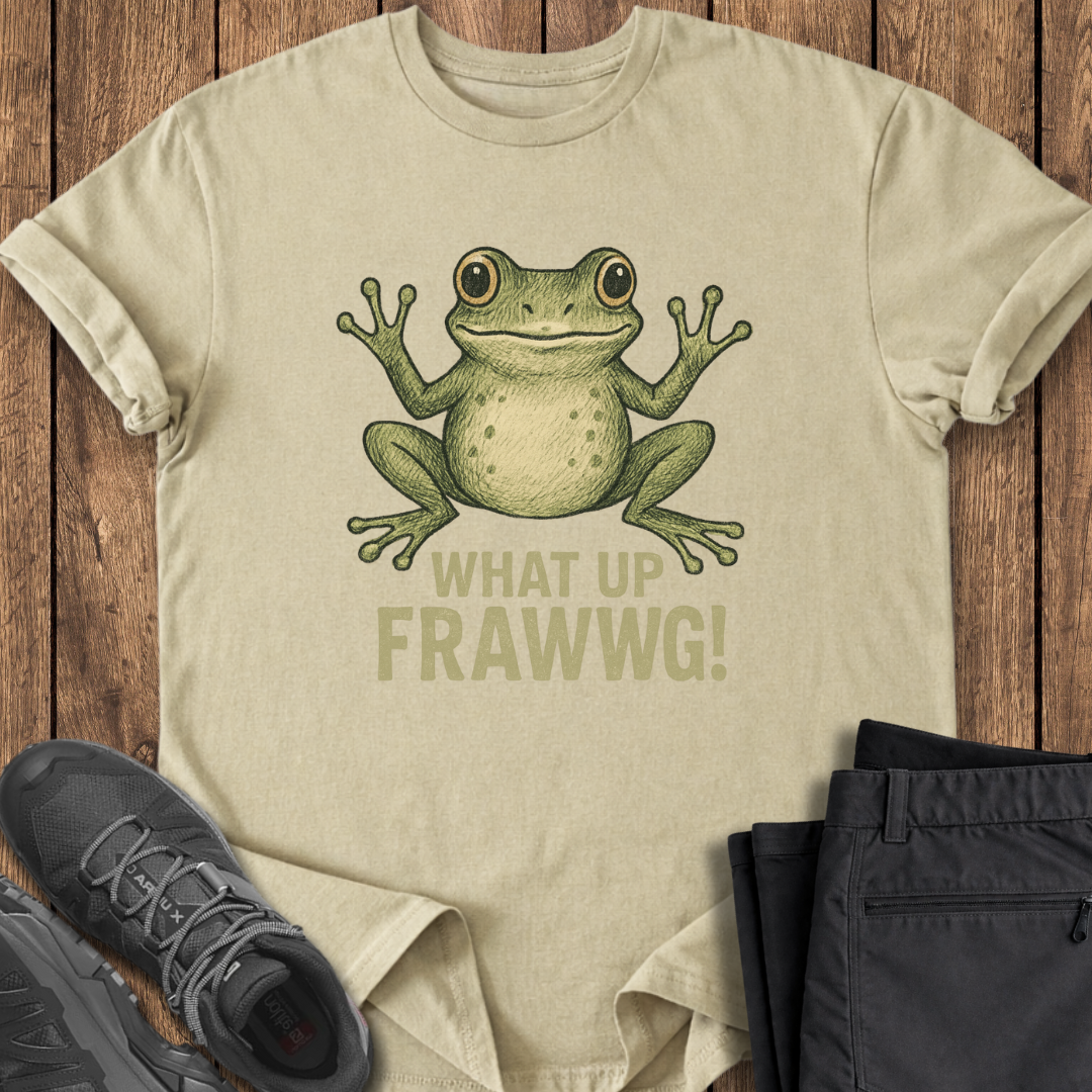 Beige t-shirt with a frog graphic and text 'WHAT UP FRAWWG!' on a wooden surface with shoes and pants.