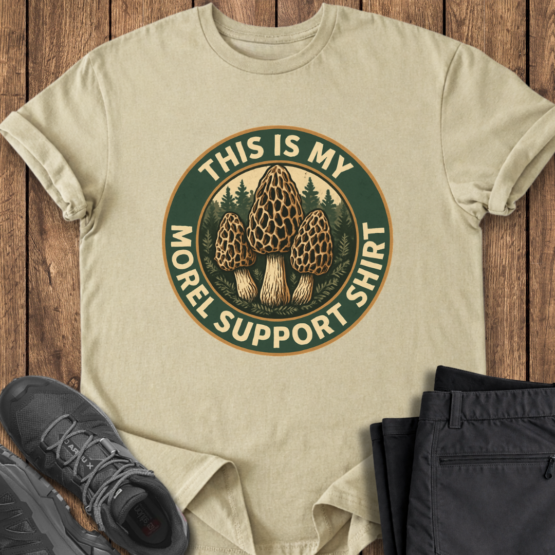 Beige t-shirt with mushroom graphic and text on a wooden surface with shoes and pants.