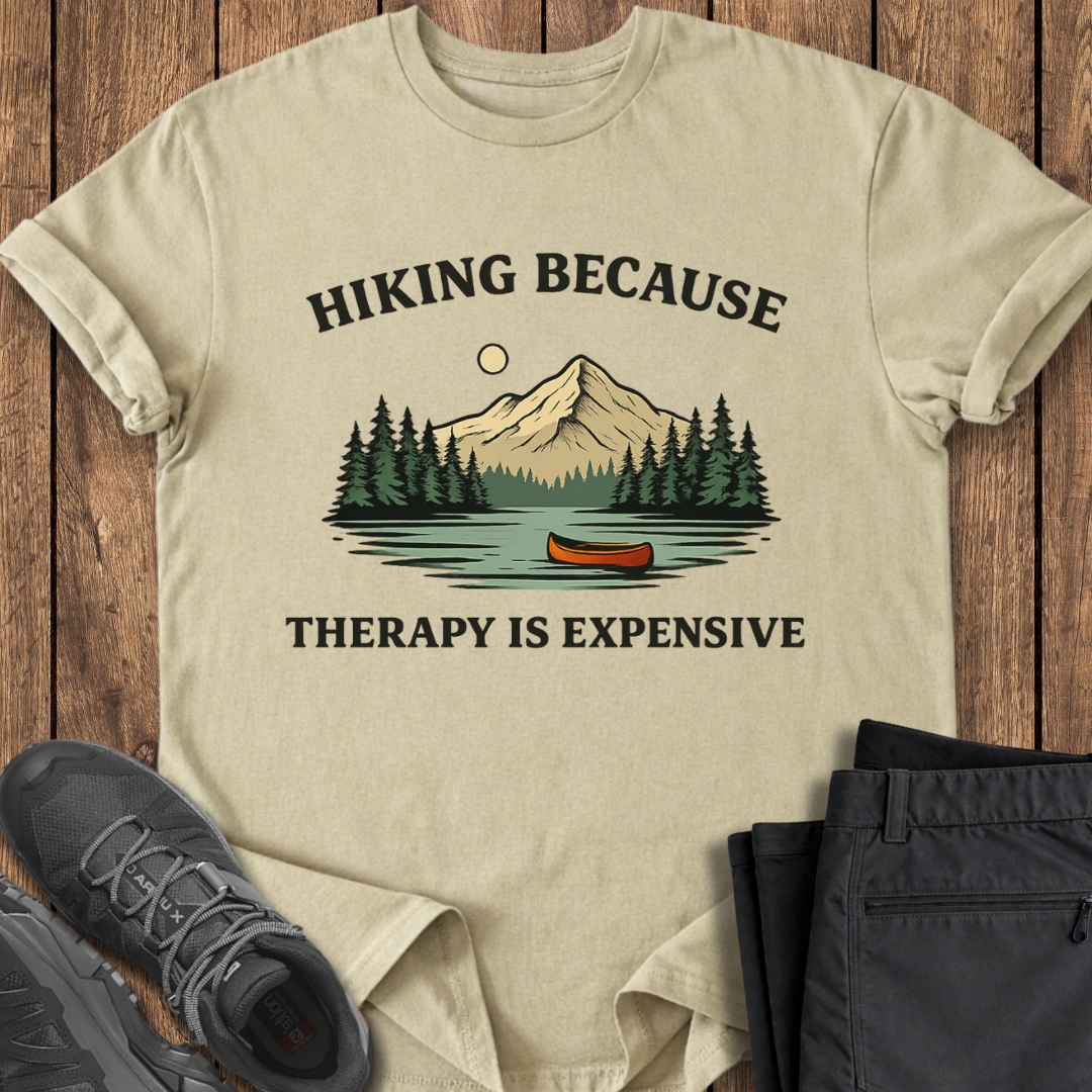 Beige t-shirt with hiking graphic and text on a wooden surface with shoes and pants. mental health outdoors shirt