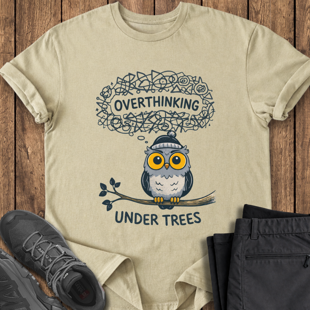 Beige t-shirt with an owl graphic and text on a wooden surface with shoes and pants. adhd hiking t shirt