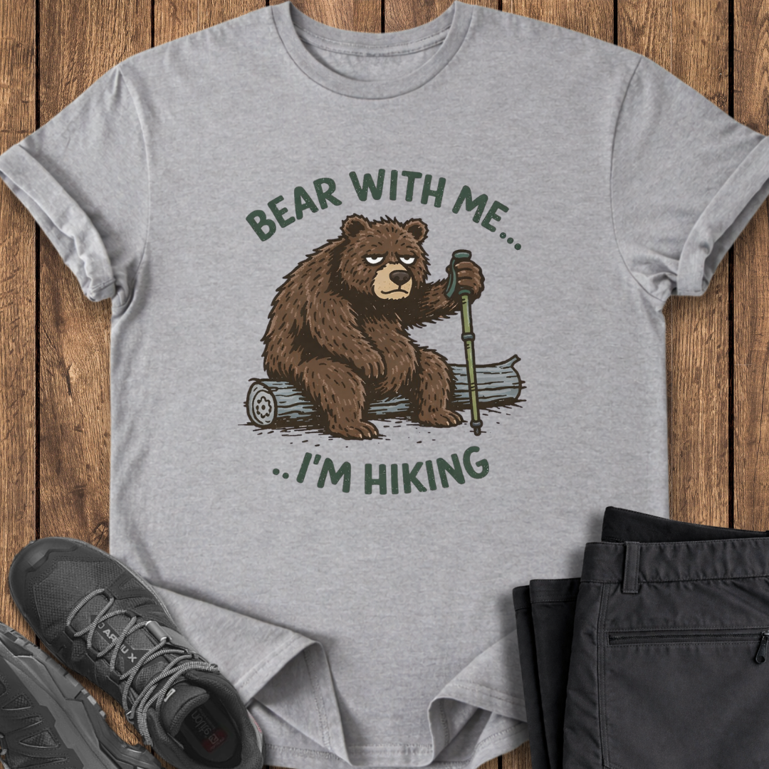 Gray t-shirt with bear graphic and text 'Bear with me... I'm hiking' on a wooden surface with hiking pole grouchy bear funny shirt