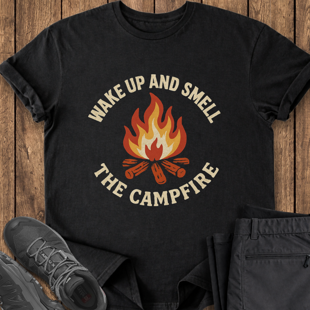 Black t-shirt with 'Wake Up and Smell the Campfire' design on a wooden surface with shoes and pants. funny camping t shirt