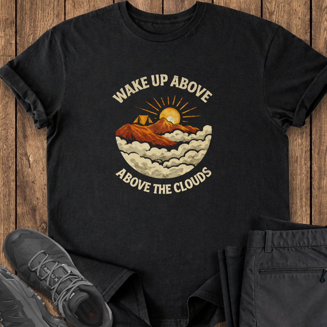Black t-shirt with mountain graphic and text 'Wake Up Above the Clouds' on a wooden surface with shoes and pants. mountaineering climbing camping t shirt