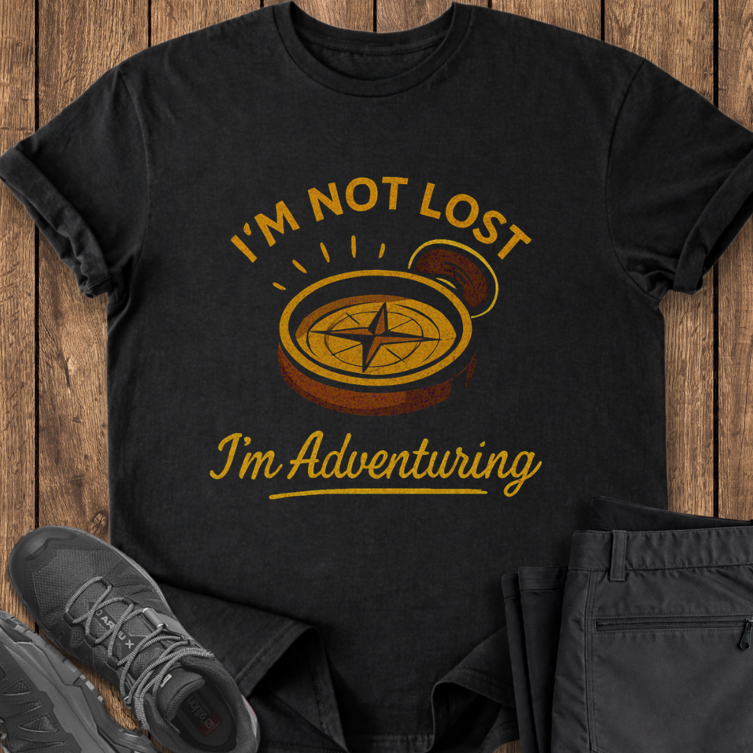 Black t-shirt with 'I'm Not Lost, I'm Adventuring' vintage compass design on a wooden surface with shoes and pants. hiking adventure t shirt