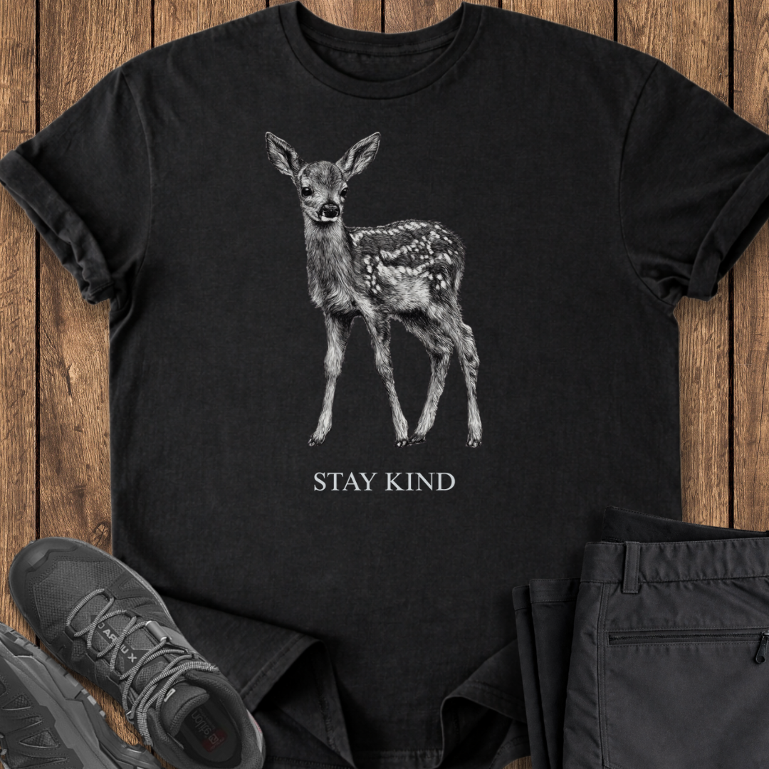 Black t-shirt with a deer graphic and 'Stay Kind' text on a wooden surface.