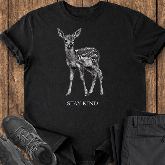 Black t-shirt with a deer graphic and 'Stay Kind' text on a wooden surface.