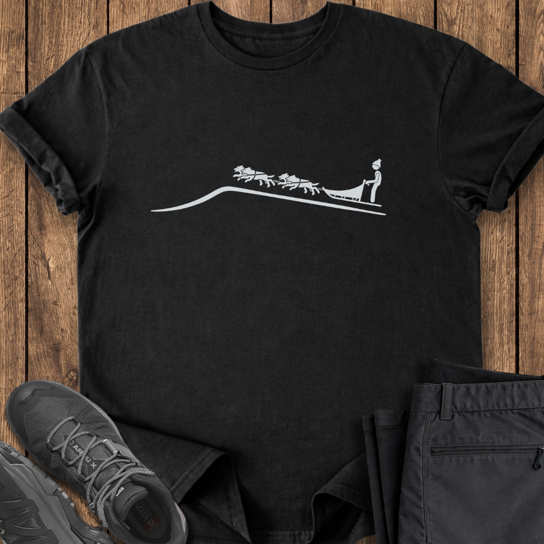 Black t-shirt with white graphic design on a wooden surface with shoes and pants. dog sledding dog sled t shirt