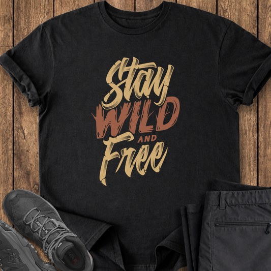 Black t-shirt with 'Stay Wild and Free' text on a wooden surface with shoes and pants.