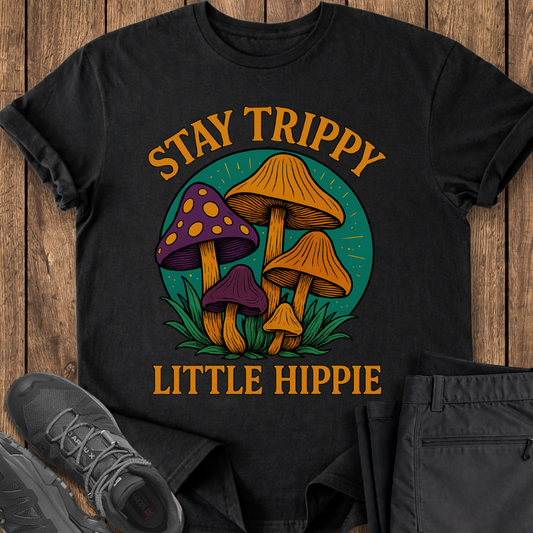 Black t-shirt with mushroom graphic and text 'Stay Trippy Little Hippie' on a wooden surface.