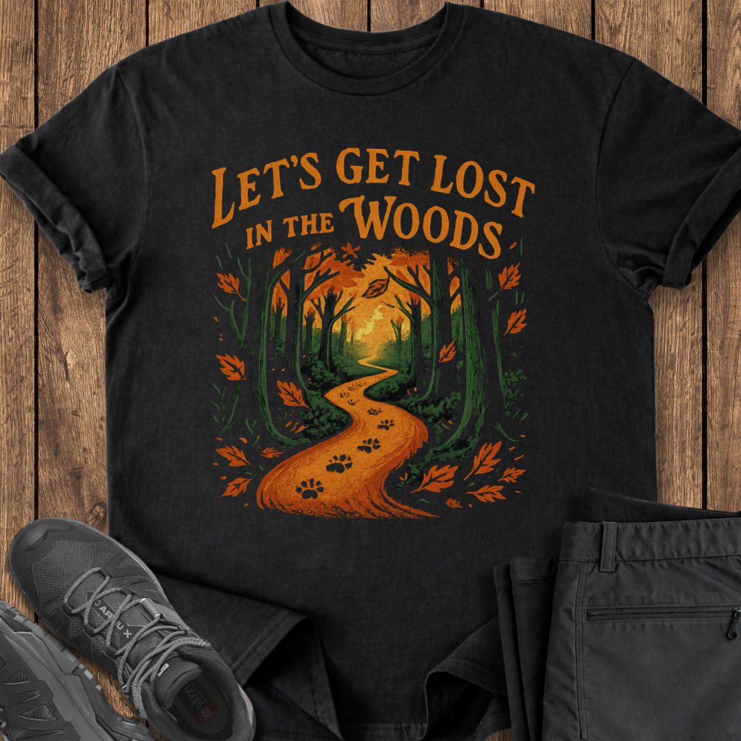 Black t-shirt with 'Let's Get Lost in the Woods' design on a wooden surface with shoes and pants.