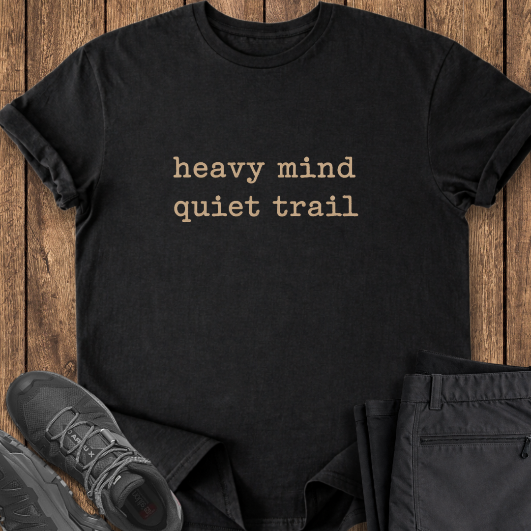 Black t-shirt with 'heavy mind quiet trail' text on a wooden surface with shoes and pants. mental health shirt