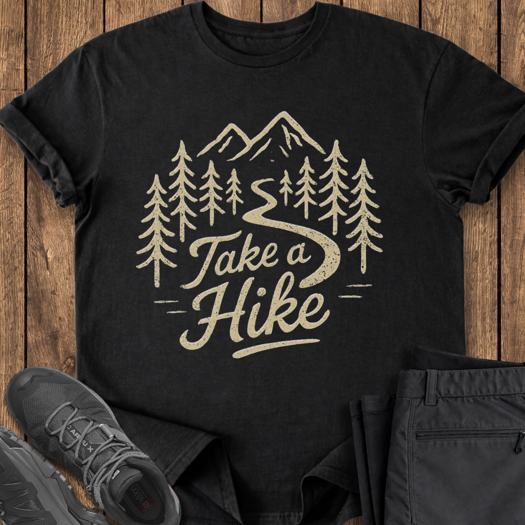 Black t-shirt with 'Take a Hike' design on a wooden surface with shoes and pants.