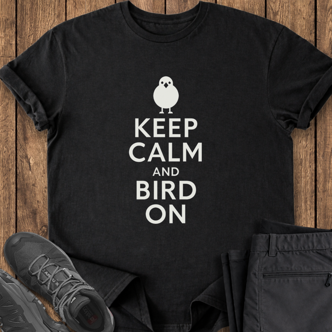 Black t-shirt with 'Keep Calm and Bird On' text on a wooden surface with shoes and pants.