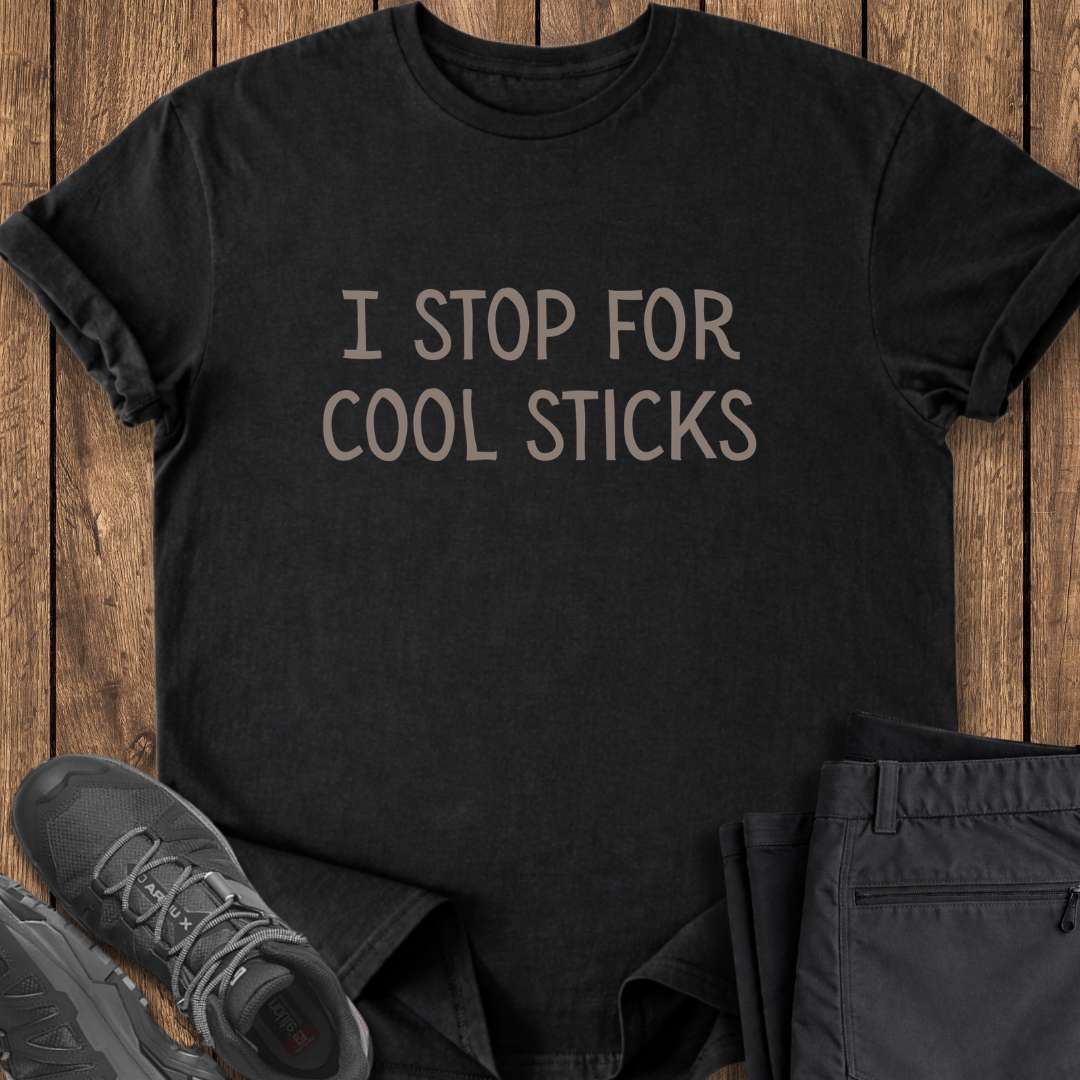Black t-shirt with 'I STOP FOR COOL STICKS' text on a wooden surface with shoes and pants. funny hiking t shirt